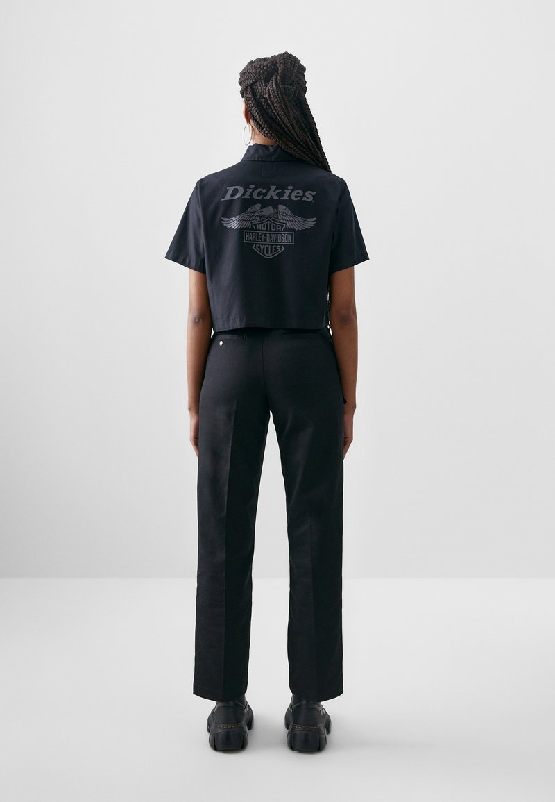 Cropped black t-shirt featuring “Dickies” logo and Harley-Davidson graphics on the back. Worn with fitted black pants and black footwear.