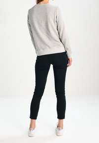 Sudadera de forro polar gris con cuello redondo y dobladillo acanalado, combinada con unos jeans ajustados negros y zapatillas blancas. Paleta de colores neutros.