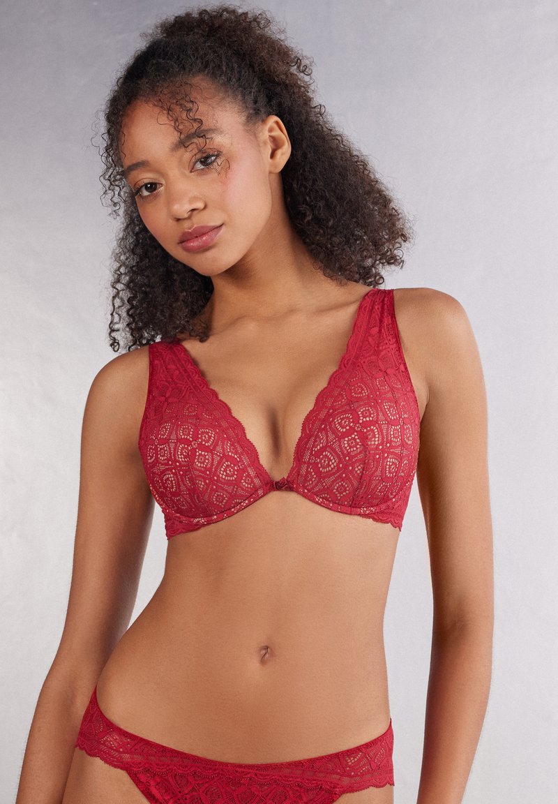 Roter Spitzen-BH und passender Bikini-Slip mit einem dreieckigen Cup-Design, gewellten Kanten und einem geometrischen Muster mit einer komplexen Textur.