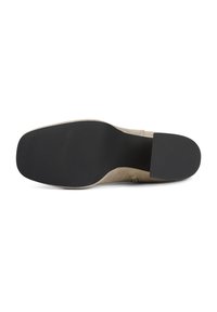 Sole di scarpa in suede beige con fondo in gomma nera liscia. Forma contornata con tacco leggermente rialzato e bordi texturizzati.