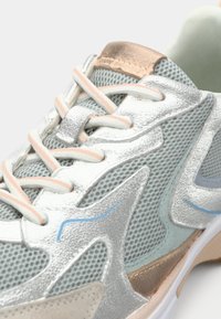 Αθλητικό παπούτσι σε ασημί με διχτυωτό ύφασμα, μπεζ και μπλε λεπτομέρειες, κείμενες επενδύσεις και κορδόνια σε αντίθεση. Στρογγυλεμένη μύτη και μαλακή σόλα.