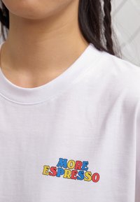 White cotton t-shirt featuring the text "MORE ESPRESSO" in bold, multicolored letters. Crew neck with standard fit and soft texture.