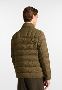 Chaquetón acolchado en verde oliva con cuello alto, diseño acolchado horizontal y textura suave. Sin logotipos visibles ni detalles adicionales.