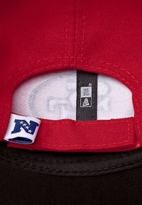Rote Kappe mit verstellbarem Riemen, die ein weißes Etikett mit einem blauen "N" und ein schwarzes Innenetikett mit dem New Era Logo zeigt.