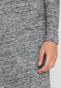 Tissu en tricot gris avec un motif texturé, mettant en avant un gros plan d'une main reposant sur le matériau, révélant une texture douce et confortable.