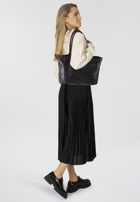 Zwarte leren totebag met twee gevlochten handvatten, voorzien van een ritsluiting en zijvak; gladde textuur en minimalistisch ontwerp.