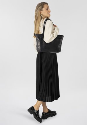 Bolsa tote de piel negra con dos asas trenzadas, que cuenta con un cierre de cremallera y un bolsillo lateral; textura suave y diseño minimalista.