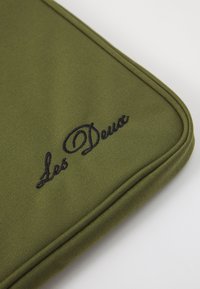 Green fabric laptop sleeve with black embroidered text "Les Deux," featuring a padded edge and textured surface.