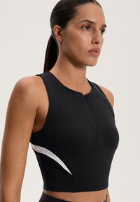 Čierny športový crop top s okrúhlym výstrihom a zipsom. Obsahuje biely akcent na boku a priliehavý strih. Hladká, elastická tkanina.