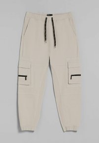 Beige cargo kalhoty s elastickým páskem, černými šňůrkami, několika kapsami a zúženými nohavicemi s elastickými manžetami.