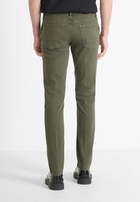 Pantalones rectos de color verde oliva con una textura suave, que cuentan con dos bolsillos traseros y cierre de botón, combinados con zapatos negros.