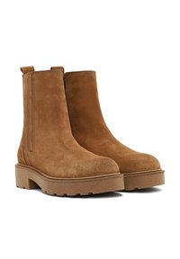Botines de ante marrón con suela gruesa, paneles laterales elásticos y pestañas de tirón. Destacan por su textura suave y diseño de punta redondeada.