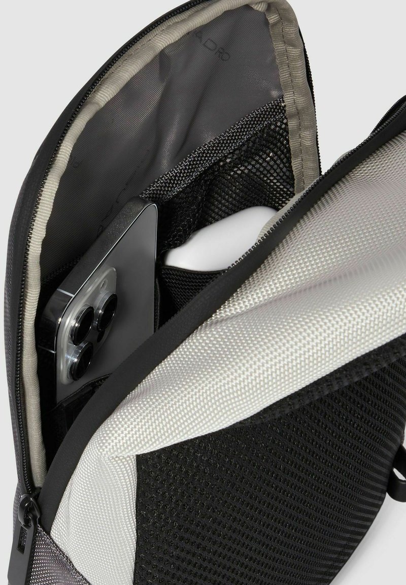 Interno della borsa nero e grigio con tasca in rete, texture liscia e con uno smartphone con custodia argentata esposto. Apertura con zip.