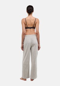 Pantalon de survêtement gris à jambes larges avec ceinture élastique, associé à un soutien-gorge foncé, vu de dos. Tissu doux et coupe décontractée.