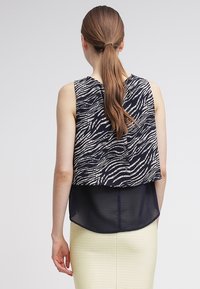 Top senza maniche con un motivo astratto a onde in blu navy e bianco, design a strati con una parte inferiore trasparente e orlo curvo.