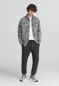 Szara koszula dżinsowa z dwiema kieszeniami na piersiach, noszona na białej koszulce; w zestawieniu z czarnymi spodniami dresowymi i szarymi sneakersami.