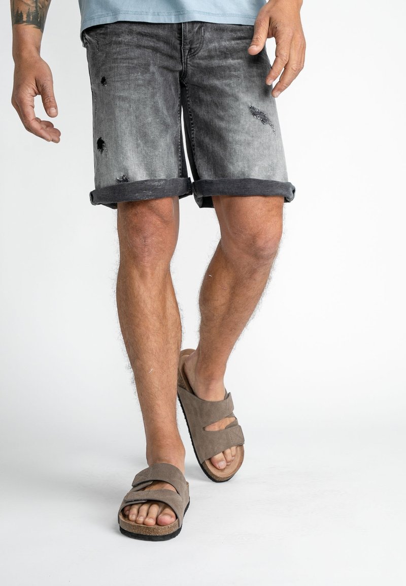 Grå denimshorts med slitna detaljer, vikta fållar, kombinerat med bruna sandaler med två remmar och en texturerad sula.