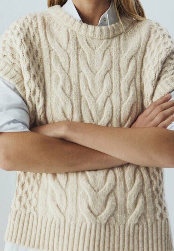 Beige kabelstickad tröja med vid halsringning, korta ärmar och ribbad fåll. Har intrikata texturerade mönster över hela.