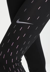 Leggings neri in materiale elastico con motivi a strisce verticali viola e grigio. Presentano un logo Nike argentato sul lato.
