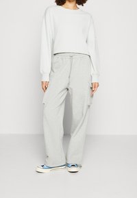 Světlé šedé cargo kalhoty s elastickým pasem a bočními kapsami, v kombinaci se světlým šedým zkráceným svetrkem a modrými teniskami.