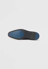 La semelle de la chaussure présente une partie supérieure lisse noire avec une section en caoutchouc texturé bleu et des accents dorés près du talon, affichant une forme arrondie.