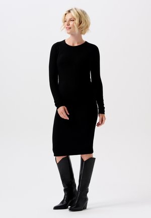 Schwarzes langärmliges Rippstrickkleid mit taillierter Silhouette und knielangem Saum, kombiniert mit knielangen schwarzen Lederstiefeln mit spitzer Zehe.