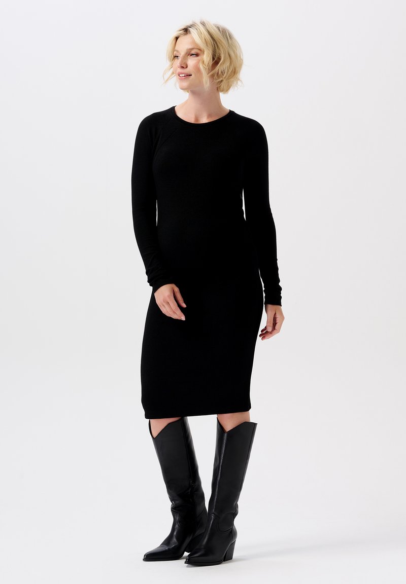 Schwarzes langärmliges Rippstrickkleid mit taillierter Silhouette und knielangem Saum, kombiniert mit knielangen schwarzen Lederstiefeln mit spitzer Zehe.