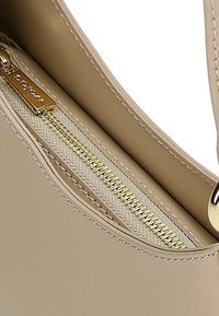 Intérieur d'un sac à main en cuir beige avec une fermeture éclair dorée et une doublure en tissu. Texture lisse avec des détails de couture contrastants.