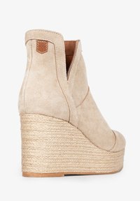Botín de ante beige con cuña envuelta en yute, diseño curvado, corte lateral y pequeña etiqueta de cuero en la parte trasera.