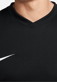Maglia sportiva nera con scollo a V, realizzata in tessuto testurizzato e presenta il logo Nike bianco a forma di swoosh sul lato sinistro in basso.