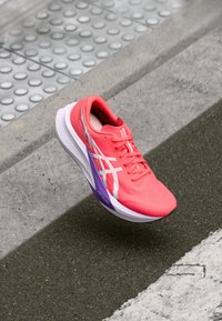 Laufschuh mit einem leuchtend korallenfarbenen Obermaterial, weißen Akzenten und einer lila-verlaufenden Sohle. Leichtes Mesh-Material mit strukturierter Oberfläche.