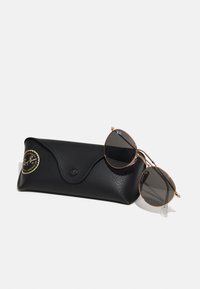 Ray-Ban pyöreät aurinkolasit tummilla linsseillä, kultaisissa metallikehyksissä ja mustassa teksturoidussa nahkakotelossa, jossa on logo.