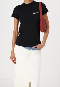 Svart bomull t-shirt med rund hals, med en vit logotyp. Kombinerad med en vit denimkjol med blå detaljer och en slits. Röd handväska.