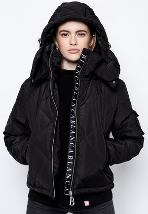 Veste matelassée noire avec capuche amovible, fermeture éclair frontale et détails de logo. Comprend des poches latérales et des poignets élastiques.