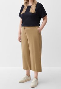 Zwart shirt met korte mouwen en tan kleurige wijde broek met zakken. Beige sneakers. Eenvoudig en casual ontwerp, lichtgewicht stof, gladde textuur.