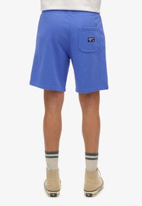 Blauwe katoenen shorts met een elastische tailleband, voorzien van een achterzak en een logo-patch, gecombineerd met beige schoenen en gestreepte sokken.