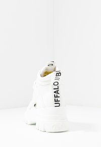 Sneaker bianco a collo alto con pelle texturizzata, logo nero a contrasto sul tallone e suola chunky bianca. La vista posteriore mostra un'etichetta di estrazione.