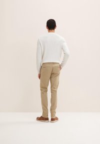 Męski jasnoszary sweter z okrągłym dekoltem, khaki spodnie i brązowe buty. Sweter ma teksturowane wykończenie; spodnie posiadają tylne kieszenie.