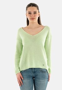 Maglione a maglia verde chiaro con scollatura a V profonda e maniche lunghe, caratterizzato da una vestibilità comoda e orlo a costine, abbinato a jeans blu.