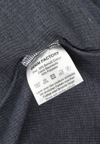 Dunkelgrauer Denimstoff mit einer strukturierten Oberfläche, ausgestattet mit einem Pflegeetikett, das Waschhinweise und Materialzusammensetzung enthält (60 % Baumwolle, 40 % Polyester).