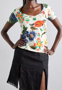 Camiseta de manga corta con flores en color crema y estampado colorido; combinada con una falda negra con aberturas laterales y dobladillo deshilachado.