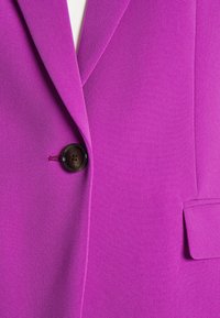 Blazer violet vif avec une fermeture par un bouton noir, un revers cranté et une poche à rabat sur le côté droit.