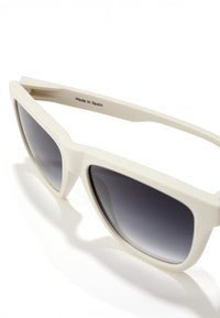 Krēmkrāsas plastmasas saulesbrilles ar pakāpeniski tumšo pelēku lēcu. Tām ir izteikta ģeometriska forma, un uz iekšējās kājiņas ir atzīme “Izgatavots Spānijā”.