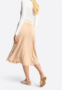 Falda midi con plisados en suave tela beige y cinturilla texturizada. Combinada con zapatos de tacón destalonados beige, mostrando una silueta relajada.