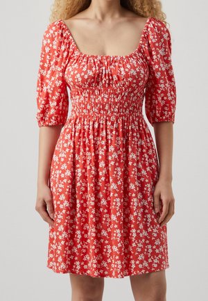 Robe rouge mi-longue à motif floral blanc, taille froncée, encolure carrée et manches bouffantes aux coudes.