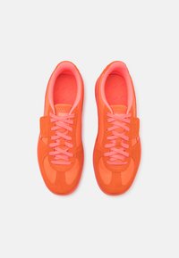 Zapatillas naranjas y rosas con una suela texturizada, material suave y cordones a juego. Presenta un logo de PUMA y una correa de seguridad en el lateral.