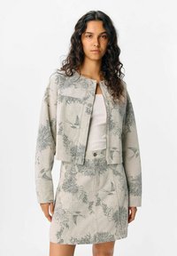 Veste courte et jupe assortie en tissu gris clair avec des motifs floraux et d'oiseaux. Dotée d'un col rond et d'une fermeture à boutons à l'avant.