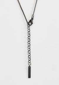 Zwart metalen halsketting met een schakeldesign. Heeft een sluiting en een rechthoekig label met gegraveerde tekst dat aan een langere kettingsegment hangt.