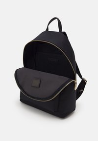 Czarny plecak z tkaniny z złotym zamkiem, pojedynczą rączką i klapą. Gładka faktura, przestronne wnętrze z dodatkową kieszenią.