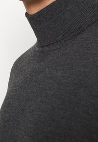 Pull à col roulé gris vu de côté, fabriqué en tissu tricoté doux et texturé avec un col haut et une coupe ajustée.